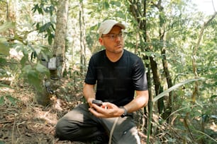 a man sitting in the woods holding a cell phone
