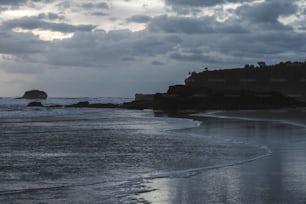 a beach with waves coming in and a rock outcropping in the distance