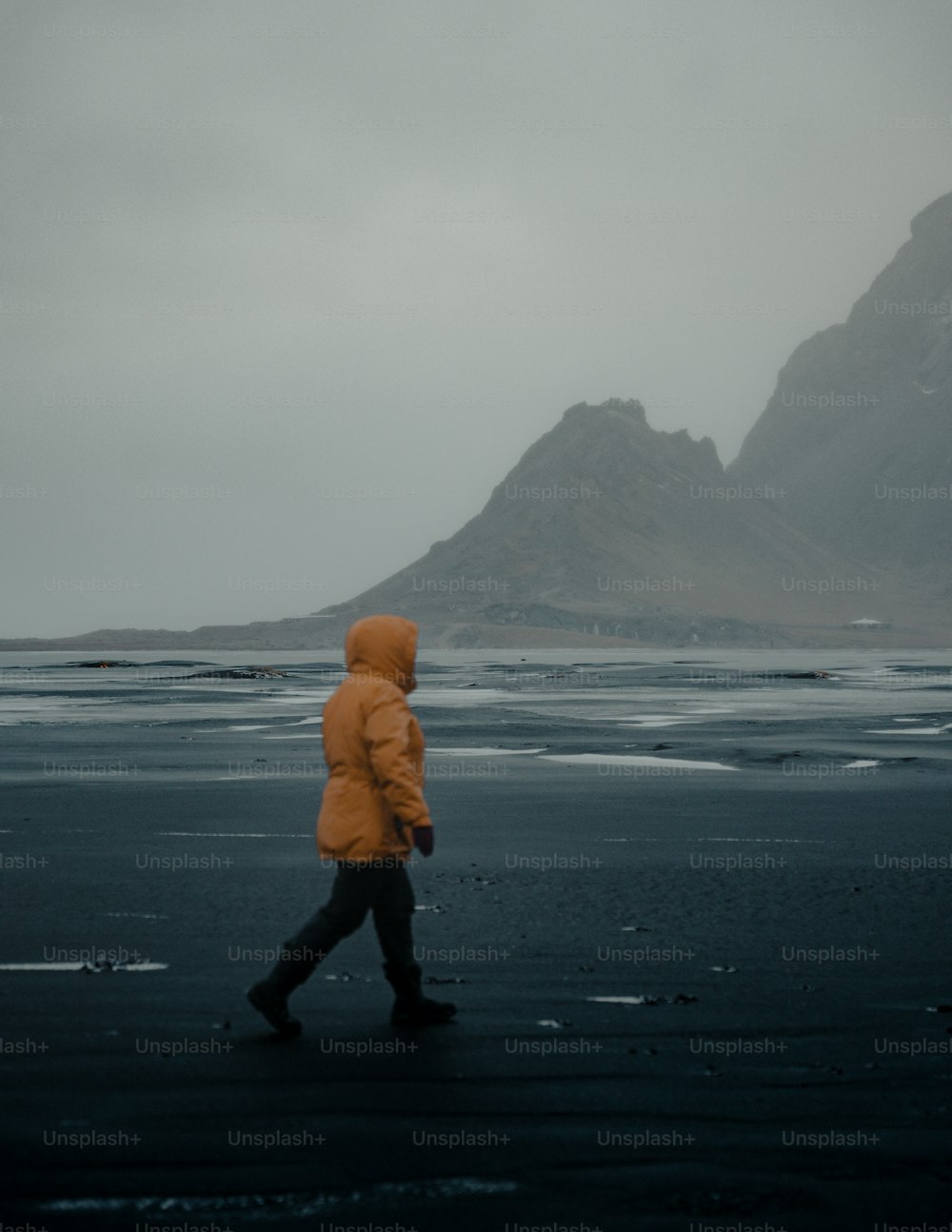 a person in a yellow jacket walking on a beach