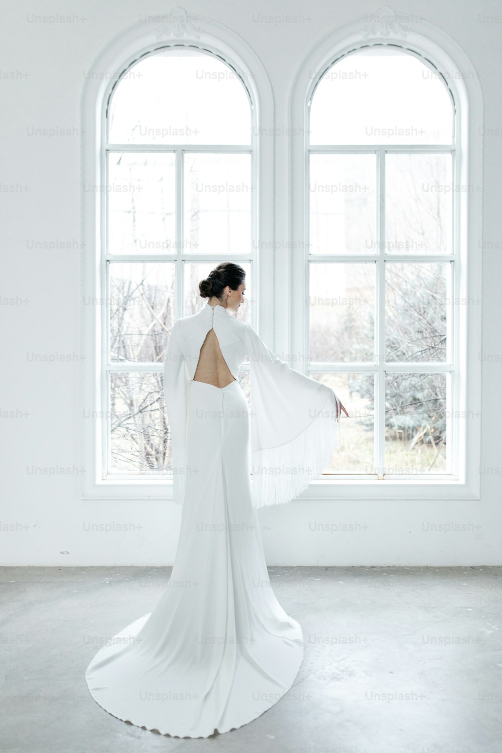 une femme en robe blanche debout devant une fenêtre