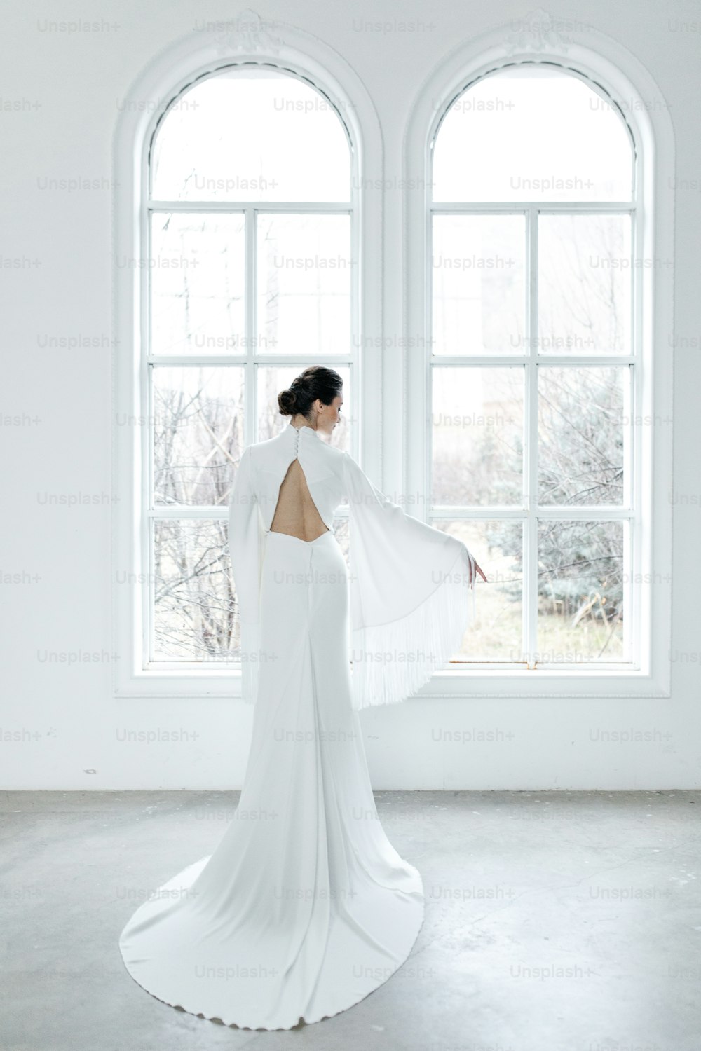 a woman in a white dress standing in front of a window