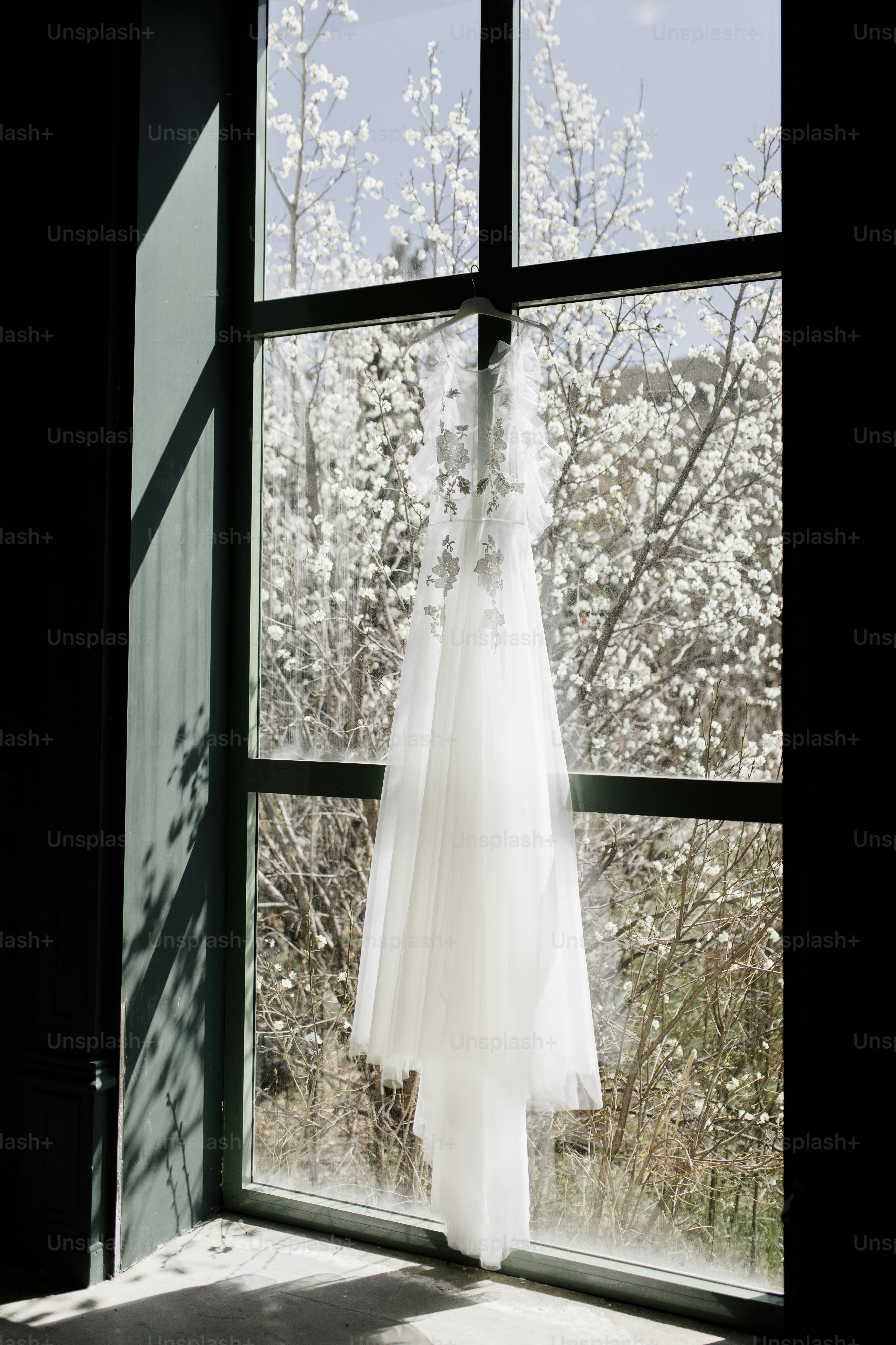 a wedding dress hanging in front of a window