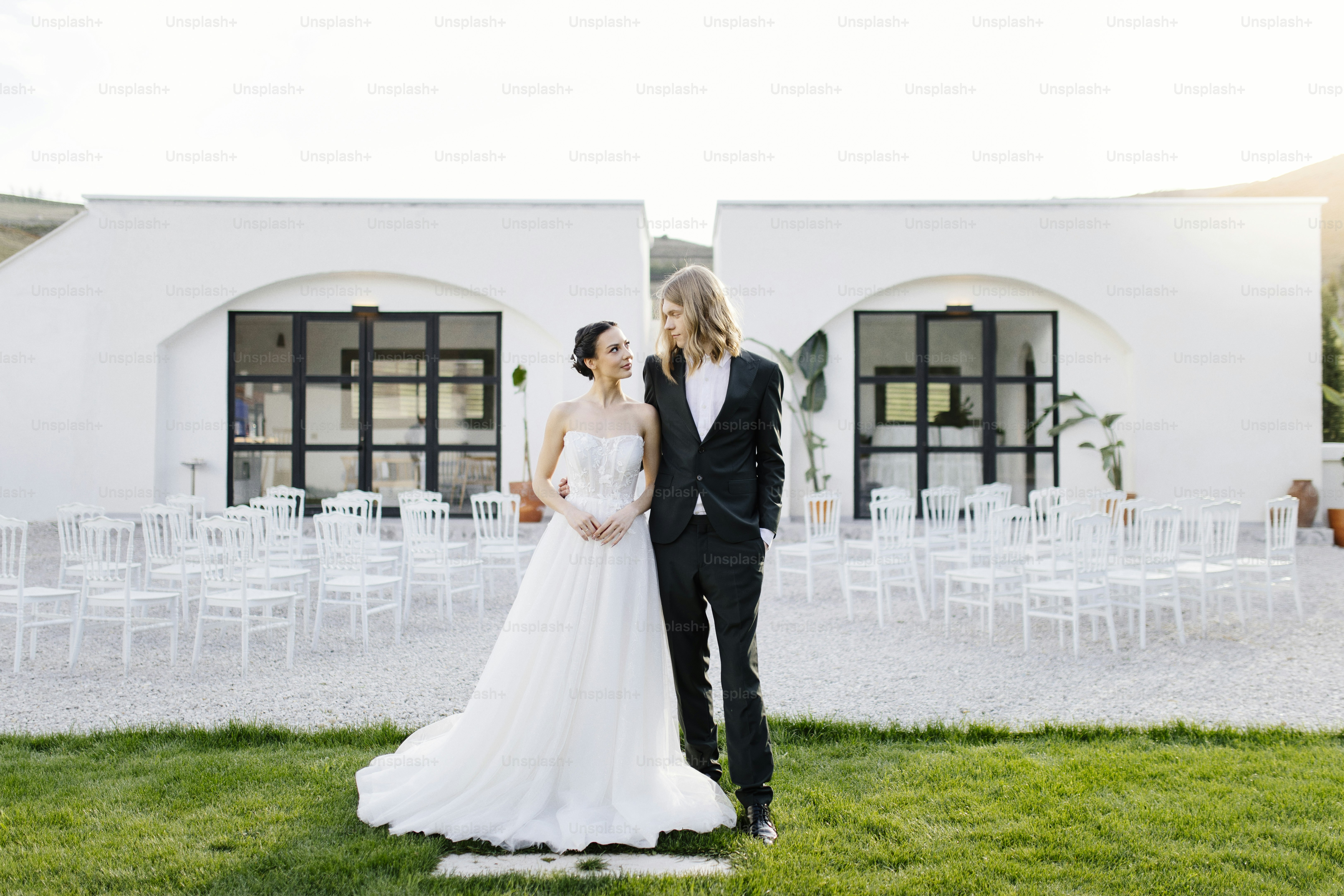 A bride and groom standing in front of a white building photo – Groom ...