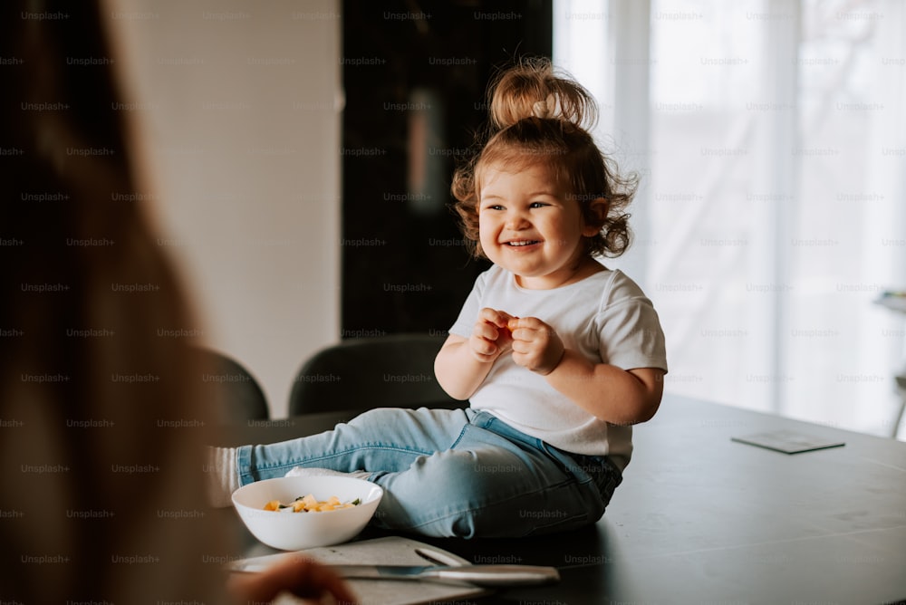 a little girl sitting on a table eating cereal