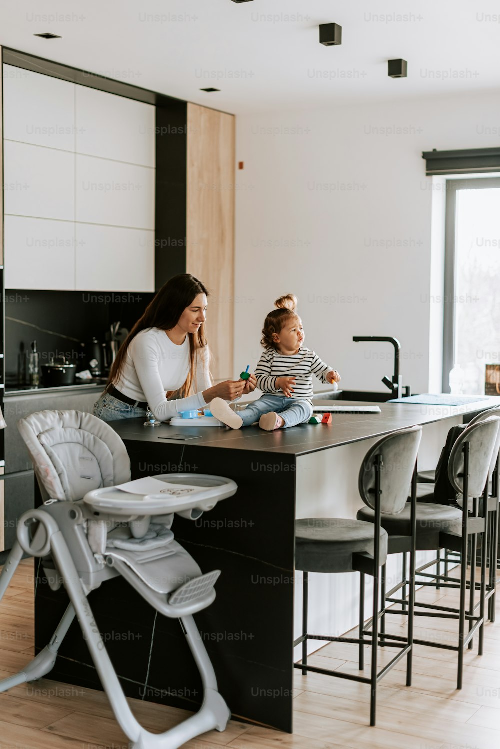 a woman sitting at a kitchen counter with a baby in a high chair