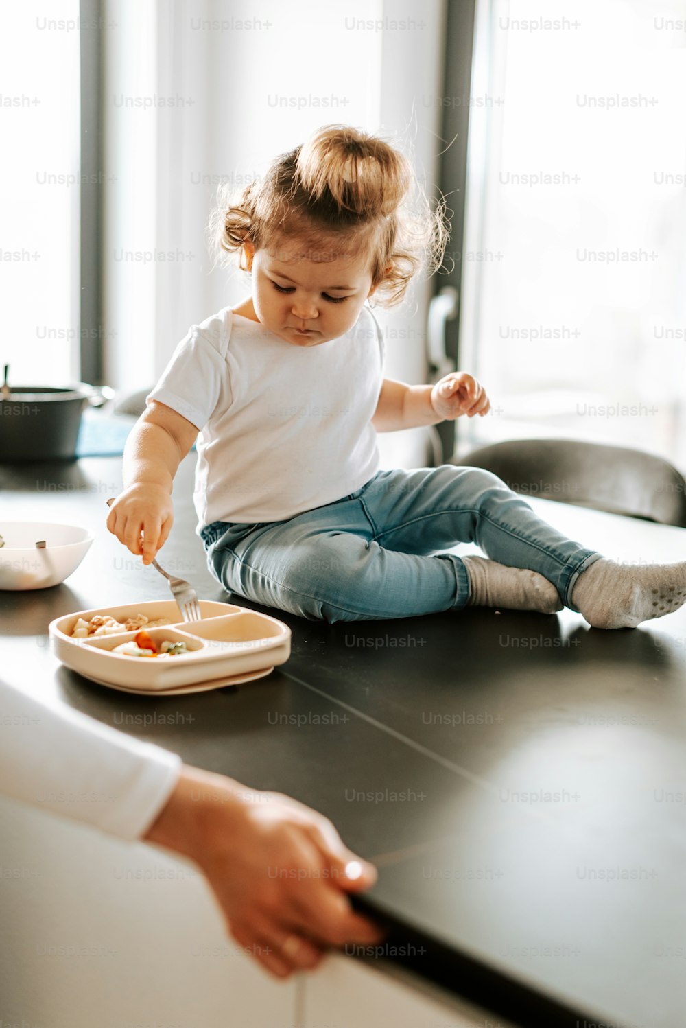 ein kleines Mädchen, das mit einem Teller Essen auf dem Boden sitzt