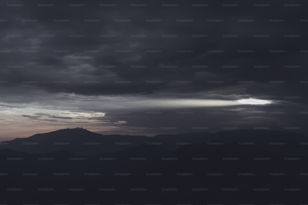 a dark sky with clouds and mountains in the background