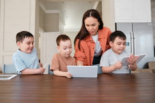 a woman and three children sitting at a table looking at a laptop