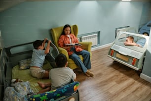 a woman sitting in a chair reading a book to children