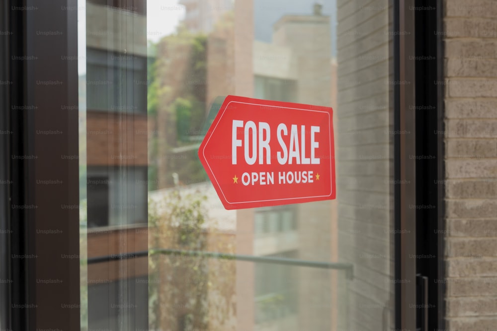 a red for sale sign sitting on the side of a window