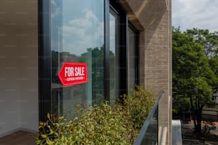 a red for sale sign sitting on the side of a building