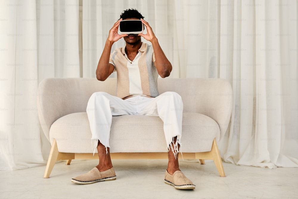 Un hombre sentado en un sofá sosteniendo un teléfono frente a su cara