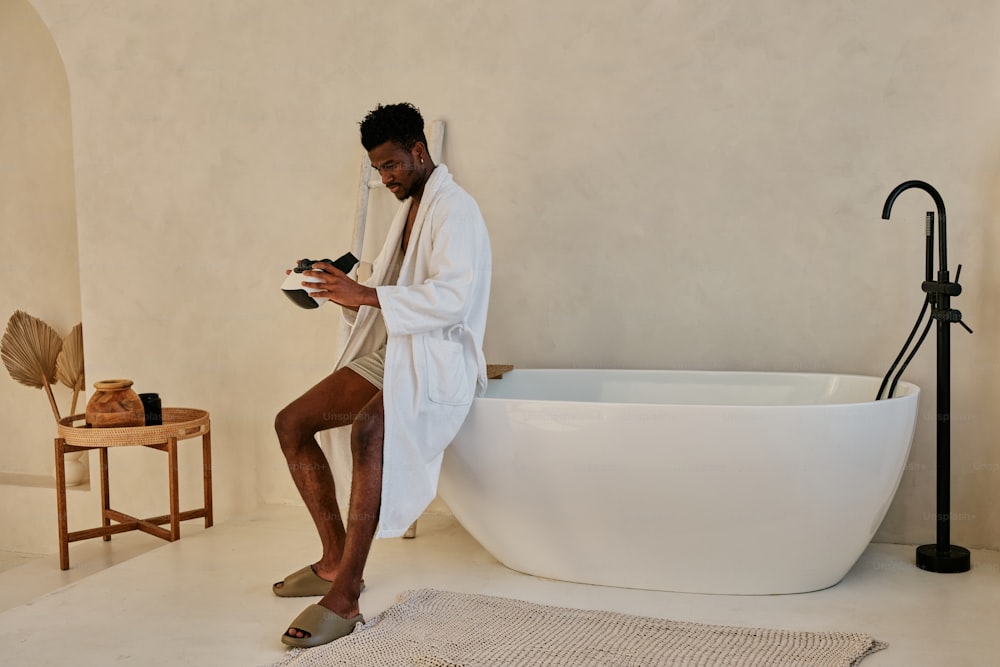 a man in a bathrobe sitting on a bathtub