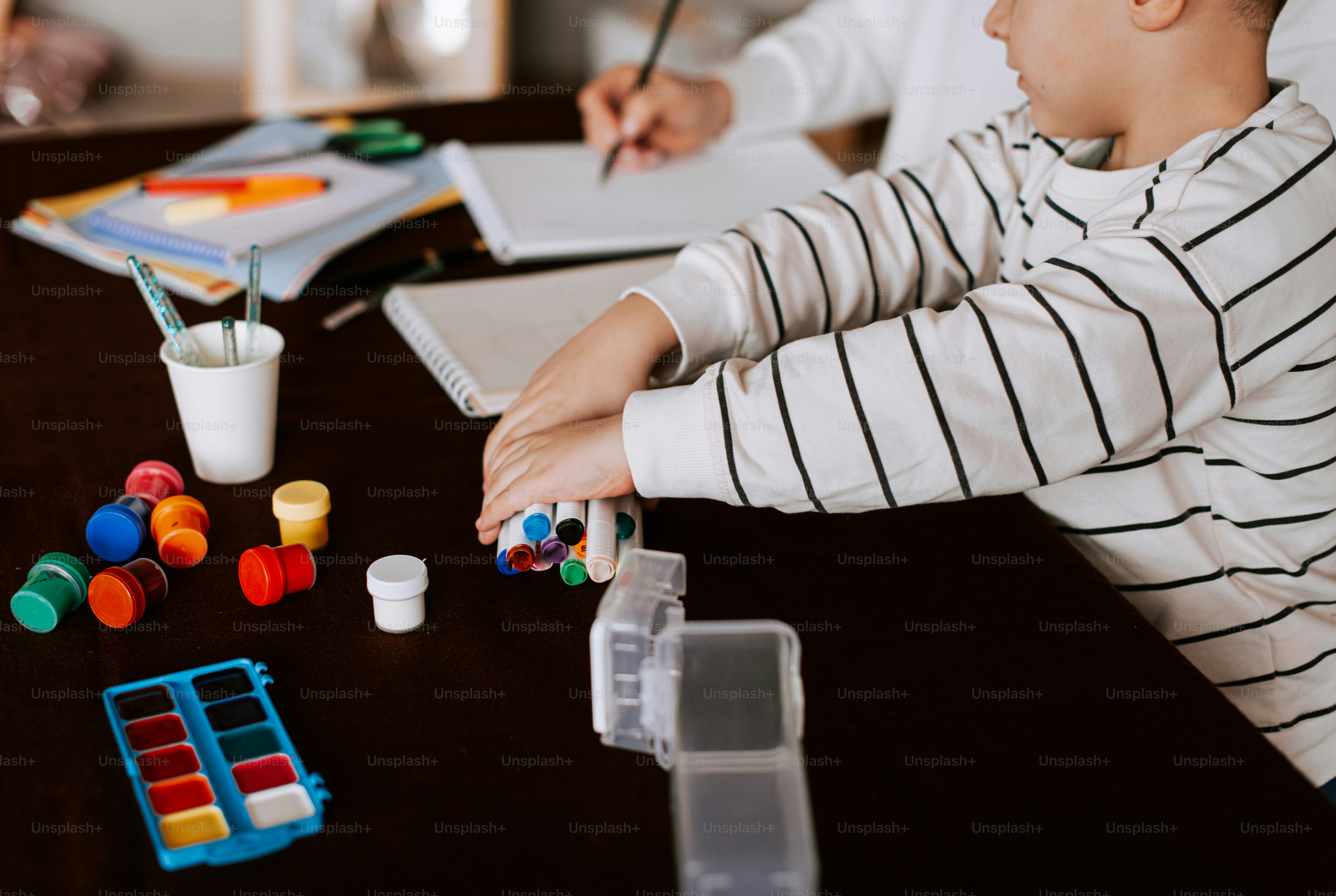 Ein kleiner Junge sitzt an einem Tisch mit Farben und Filzstiften