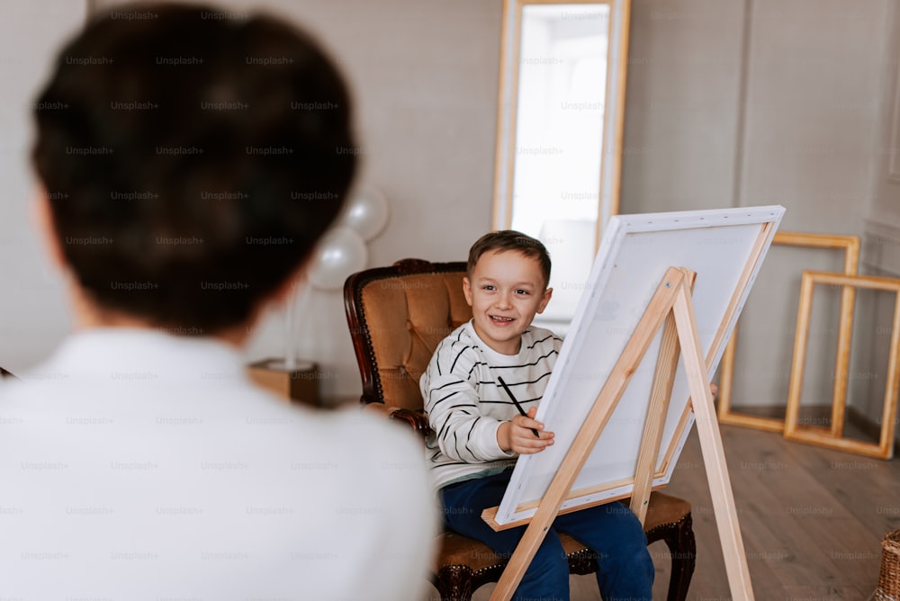 a young boy sitting in a chair in front of a easel