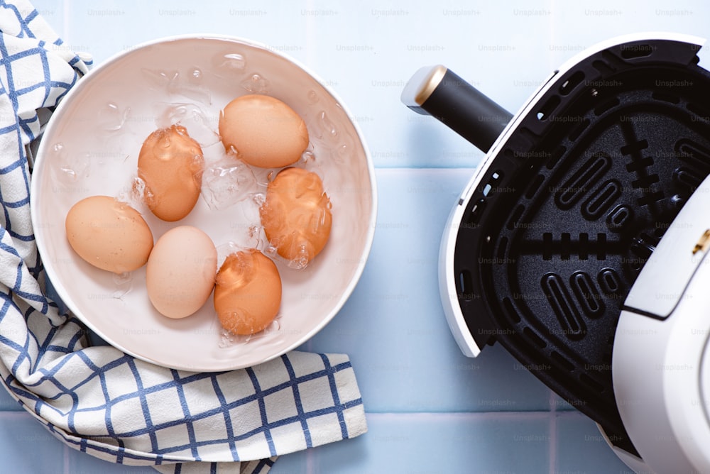 a white bowl filled with brown eggs next to an air fryer