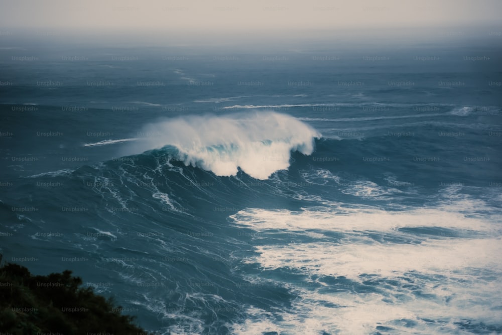 a large wave crashing into the ocean on a cloudy day