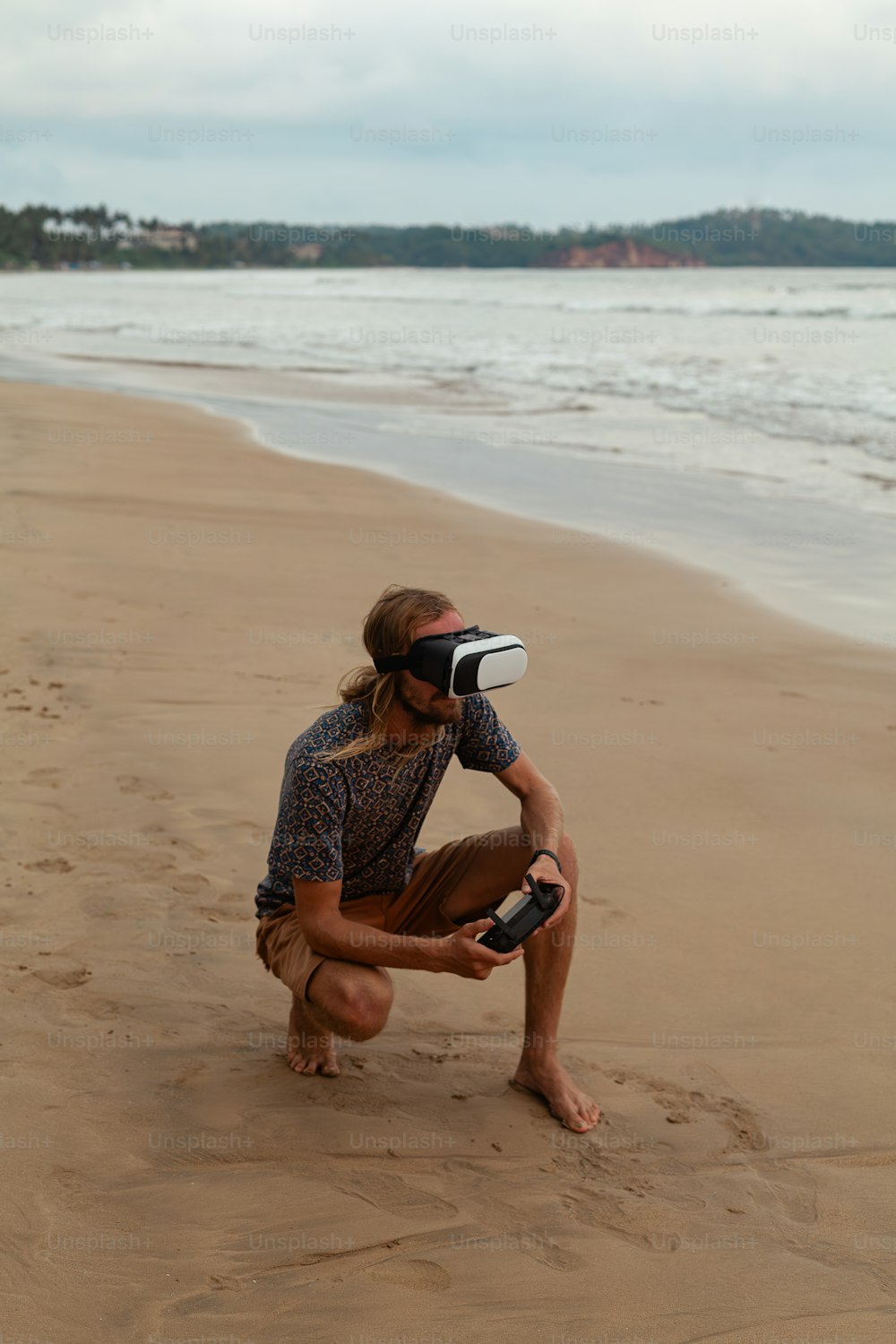 a man kneeling down on a beach holding a camera