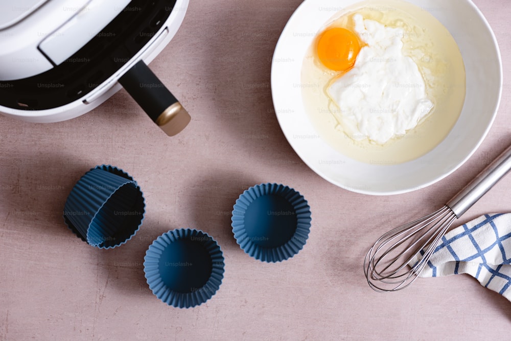 a bowl of yogurt, a whisk, and three blue cups