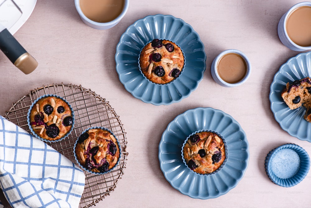 una mesa cubierta con platos de muffins de arándanos y tazas de café