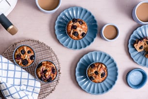 a table topped with plates of blueberry muffins and cups of coffee