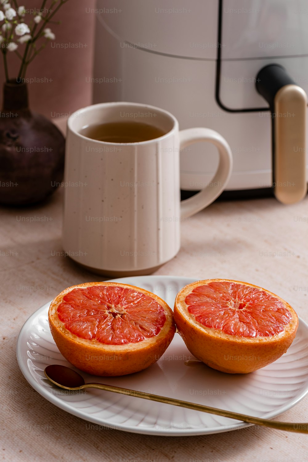 two grapefruit halves on a plate next to a cup of tea