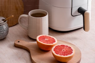 a grapefruit cut in half on a cutting board next to a cup of