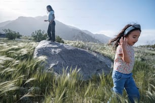 a little girl standing on top of a rock while talking on a cell phone