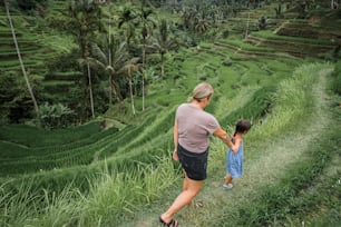 a woman and a little girl walking through a lush green field