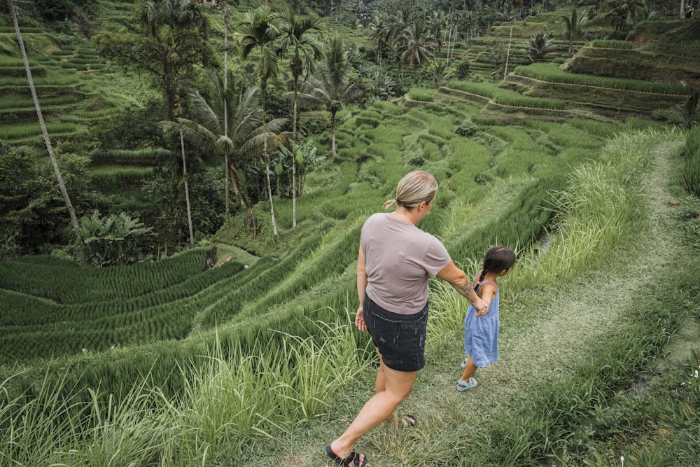 a woman and a little girl walking through a lush green field