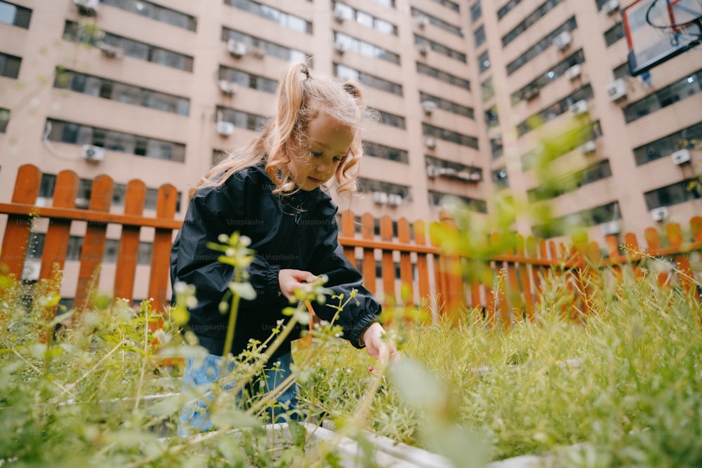 a little girl standing in the grass in front of a tall building