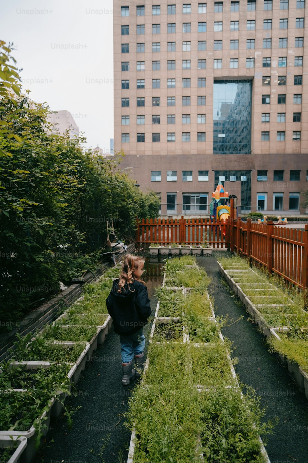 높은 건물 앞 정원을 걷고 있는 어린 아이