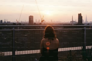 una mujer sentada en una valla mirando la ciudad