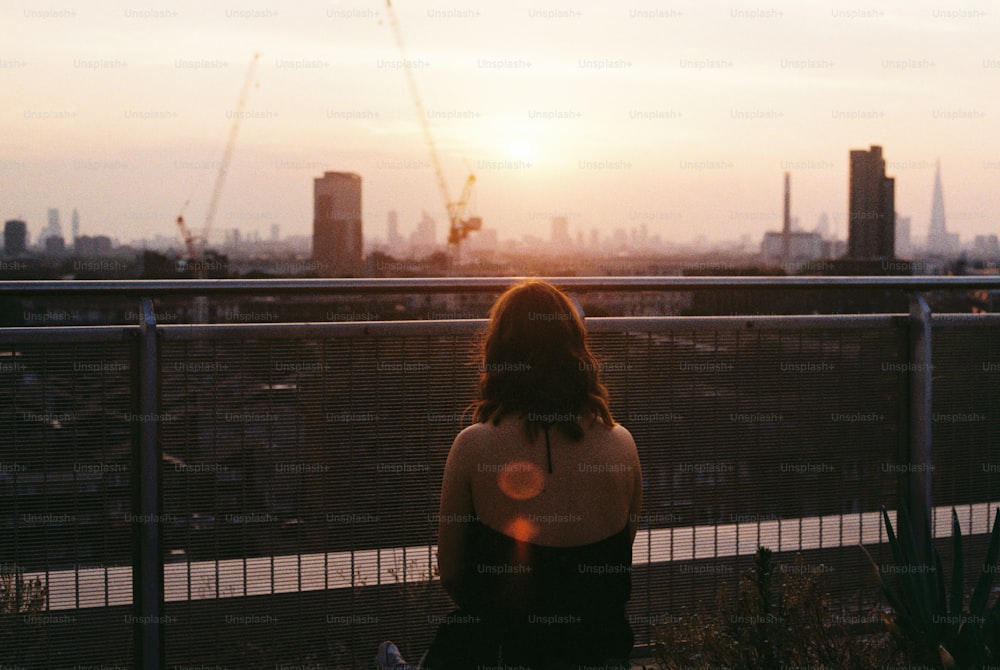 a woman sitting on a fence looking at the city