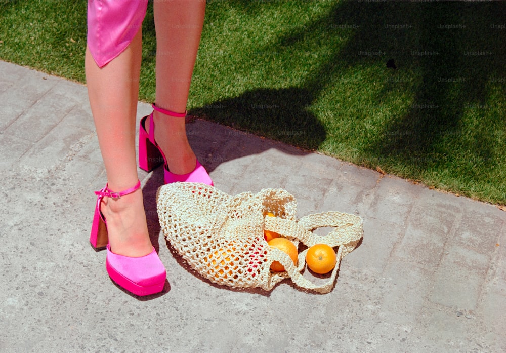 a woman's legs in pink shoes next to a bag of fruit