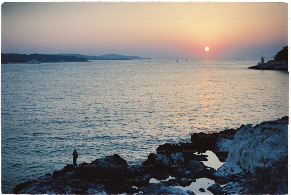 uma pessoa em pé em uma costa rochosa observando o pôr do sol