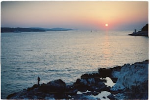 une personne debout sur un rivage rocheux regardant le soleil se coucher