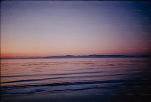 une vue d’une plage au coucher du soleil avec une montagne au loin