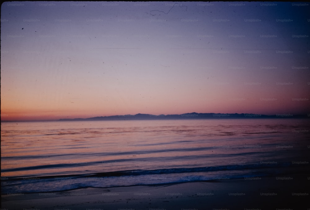 a view of a beach at sunset with a mountain in the distance
