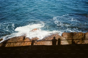 a couple of people standing on top of a cliff next to the ocean