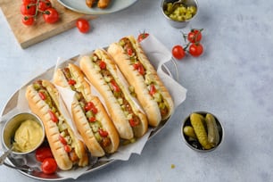 a bunch of hot dogs on a plate with pickles and tomatoes