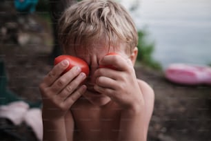 a young boy holding a tomato in front of his face