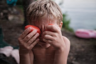 un jeune garçon tenant une tomate devant son visage