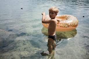 a young boy standing in the water with a donut in his hand