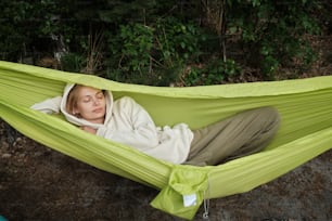 une femme allongée dans un hamac vert, les yeux fermés