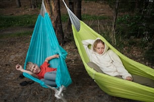 a woman sitting in a hammock next to a boy