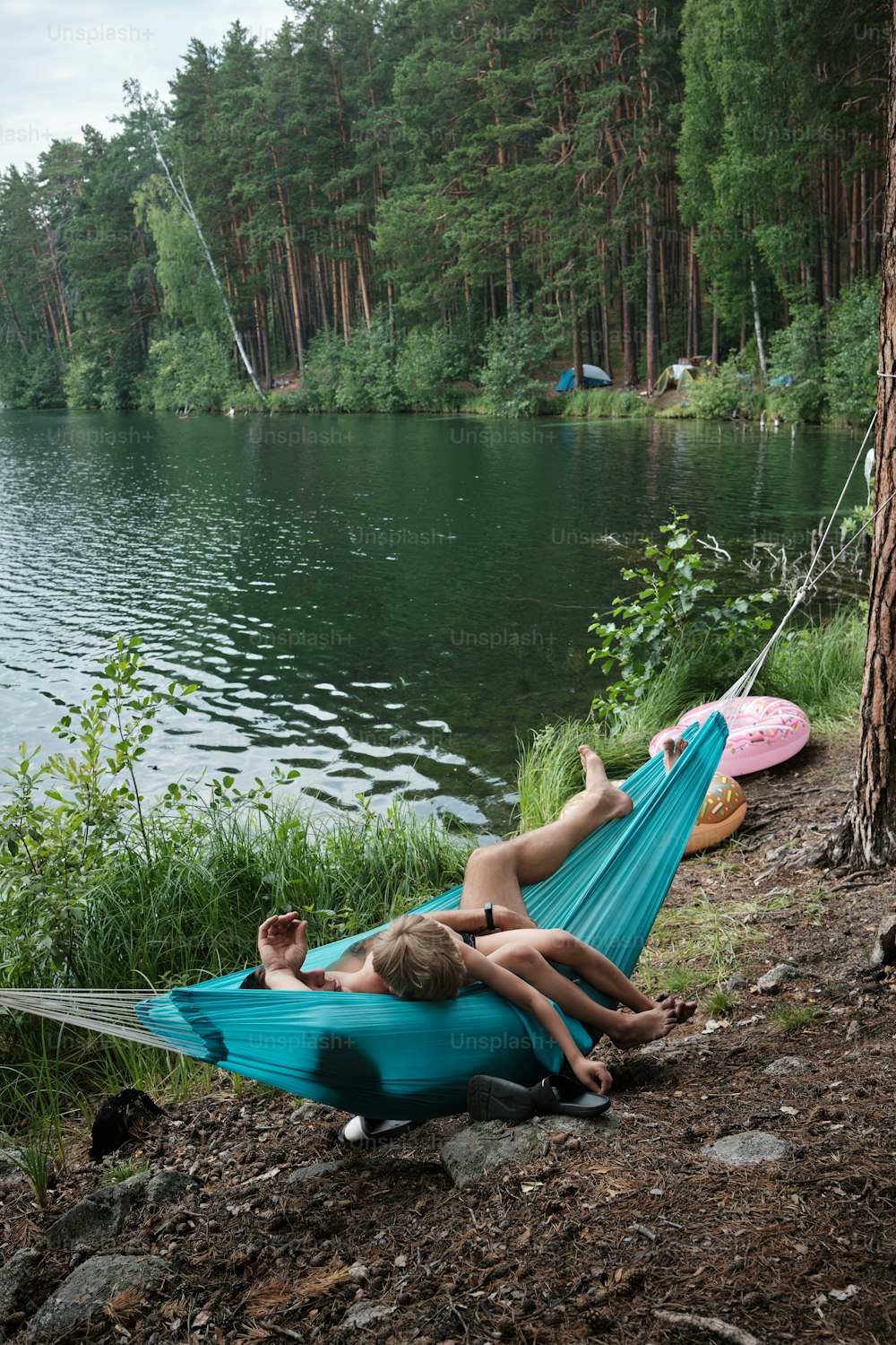 two people laying in a hammock by a lake