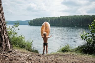 um menino segurando uma prancha de surf sobre um corpo de água