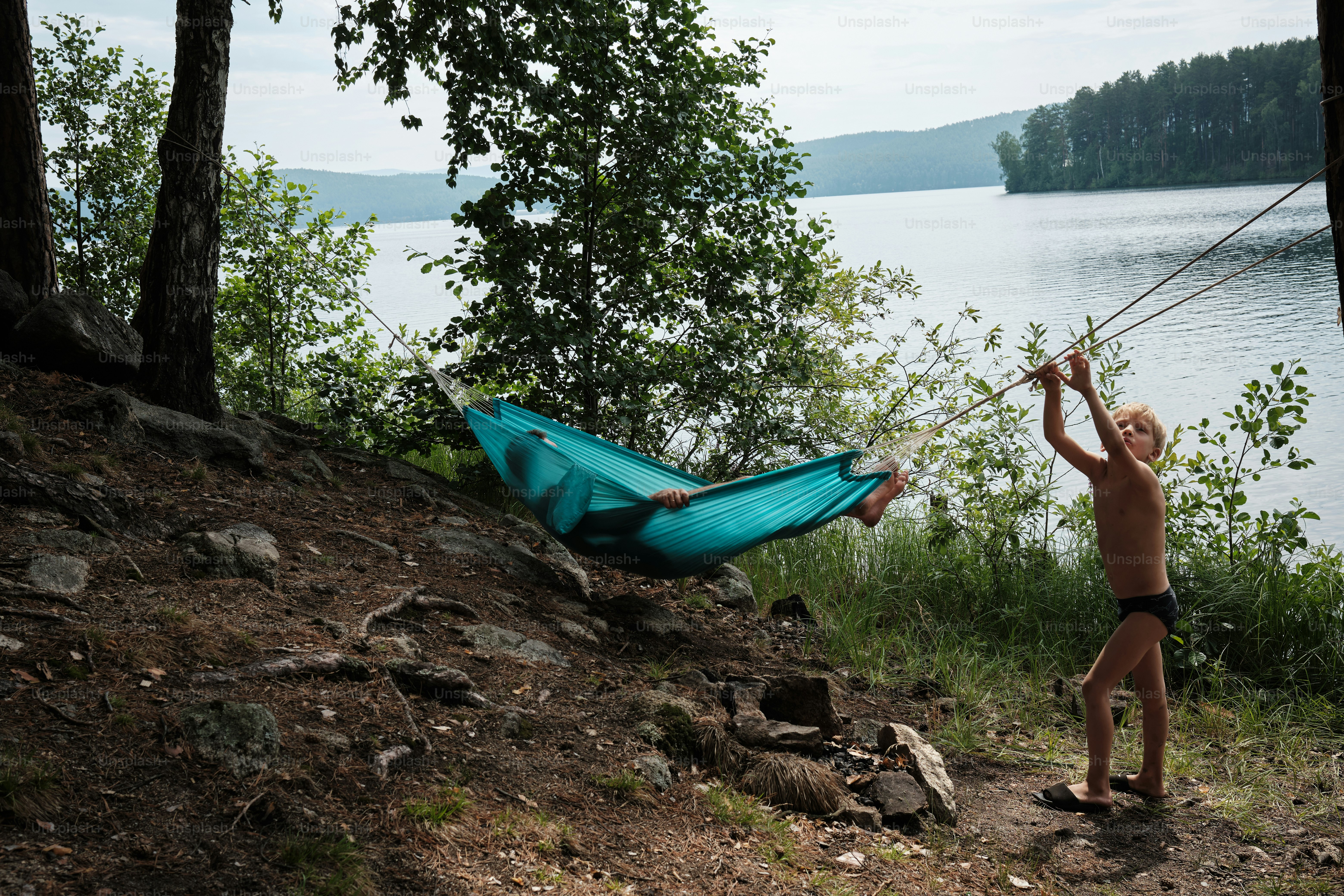 a little boy standing next to a blue hammock