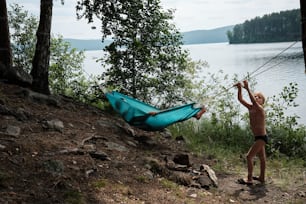 a little boy standing next to a blue hammock